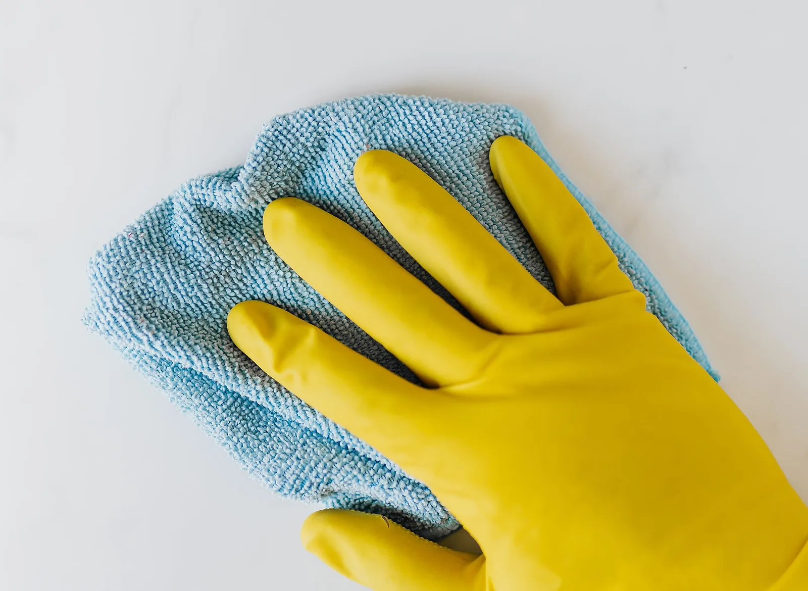 A hand in a yellow rubber glove wiping a white surface with a blue microfibre cloth